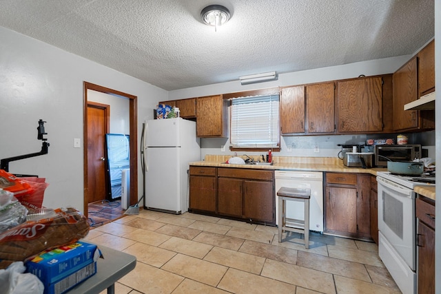 kitchen featuring white appliances, brown cabinets, light countertops, under cabinet range hood, and a sink