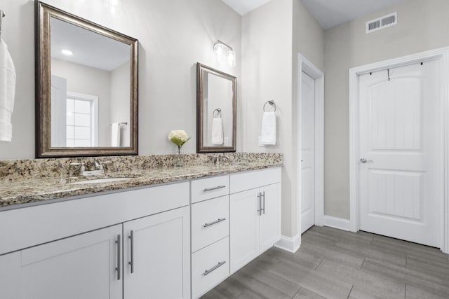 bathroom with double vanity, wood finished floors, a sink, and visible vents