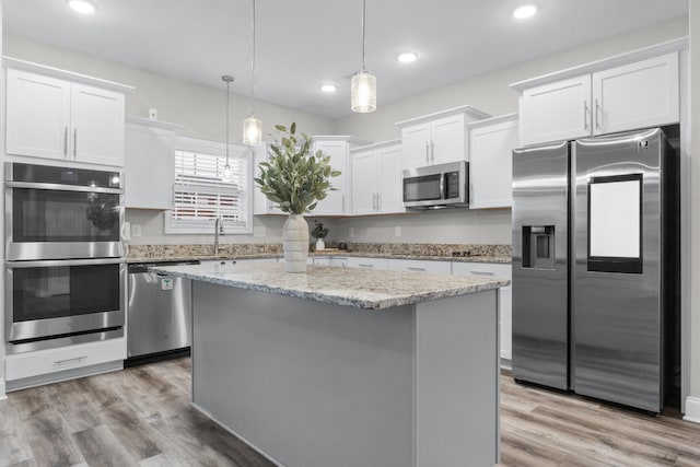 kitchen featuring white cabinetry, appliances with stainless steel finishes, light wood-type flooring, a center island, and decorative light fixtures