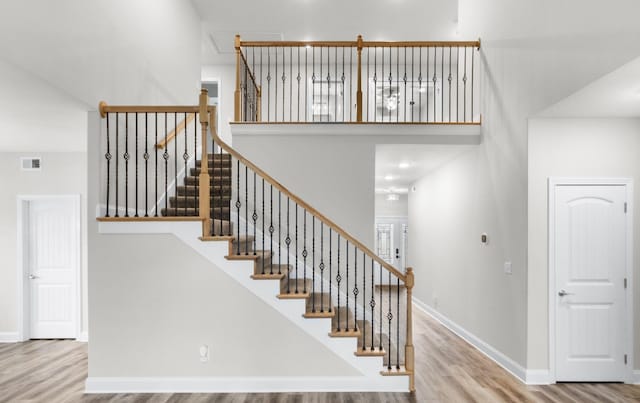 stairway with baseboards, a high ceiling, visible vents, and wood finished floors