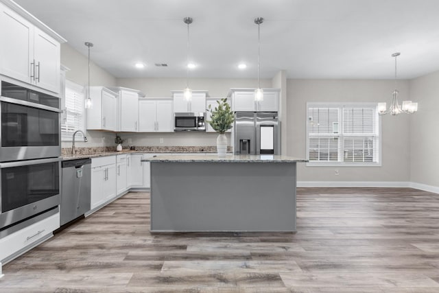 kitchen featuring stainless steel appliances, light wood finished floors, a sink, and a center island