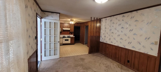 corridor with a wainscoted wall, wooden walls, ornamental molding, and wallpapered walls