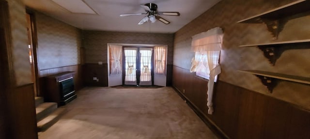 interior space featuring wainscoting, a glass covered fireplace, a ceiling fan, and wallpapered walls