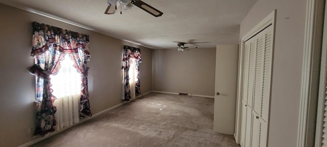 carpeted empty room featuring a textured ceiling, a ceiling fan, and baseboards