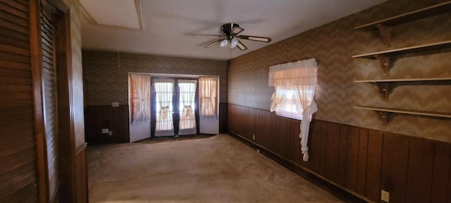 interior space with ceiling fan, light colored carpet, french doors, wainscoting, and wallpapered walls