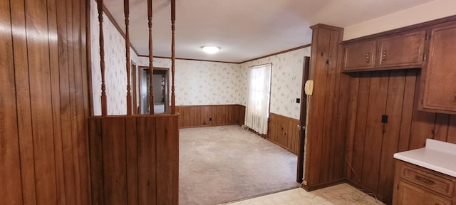 kitchen with wallpapered walls, wainscoting, light countertops, crown molding, and wood walls