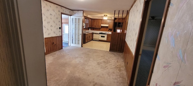 kitchen featuring under cabinet range hood, a wainscoted wall, light carpet, electric range, and wallpapered walls