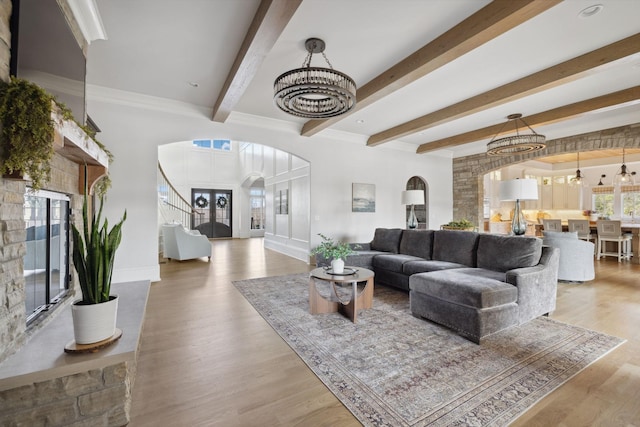 living area with baseboards, arched walkways, wood finished floors, an inviting chandelier, and beam ceiling