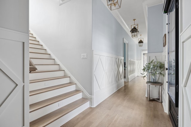 corridor featuring a wainscoted wall, a decorative wall, stairway, ornamental molding, and wood finished floors