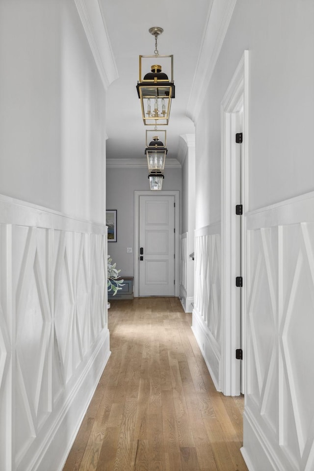 corridor with ornamental molding, wainscoting, light wood-style floors, and an inviting chandelier