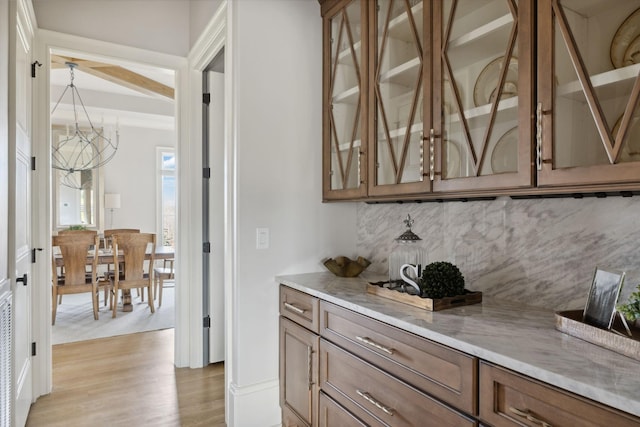 bar featuring light wood-type flooring, tasteful backsplash, and a chandelier