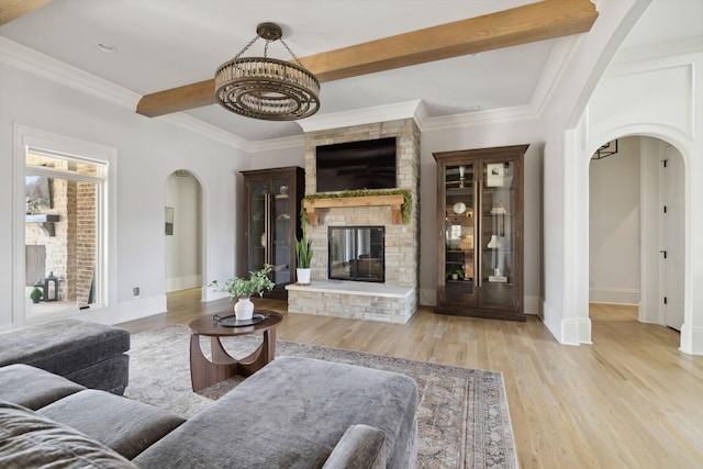 living area featuring arched walkways, beam ceiling, a fireplace, ornamental molding, and wood finished floors