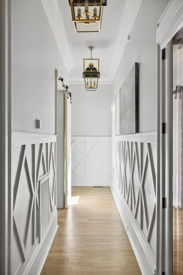 hallway with a barn door, a decorative wall, wood finished floors, visible vents, and ornamental molding