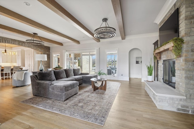 living room featuring arched walkways, a fireplace, light wood finished floors, beamed ceiling, and baseboards