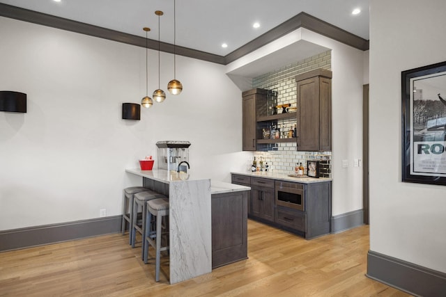 bar with light wood-style flooring, indoor bar, tasteful backsplash, stainless steel microwave, and crown molding