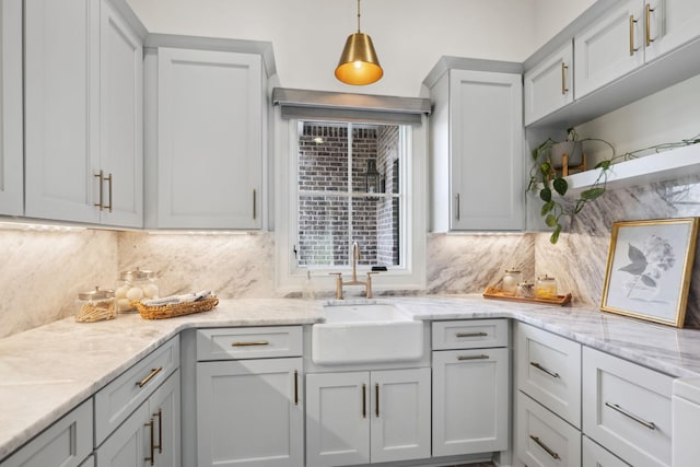 kitchen with decorative light fixtures, open shelves, decorative backsplash, a sink, and light stone countertops