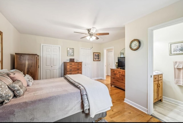 bedroom featuring light wood finished floors, two closets, a ceiling fan, ensuite bath, and baseboards