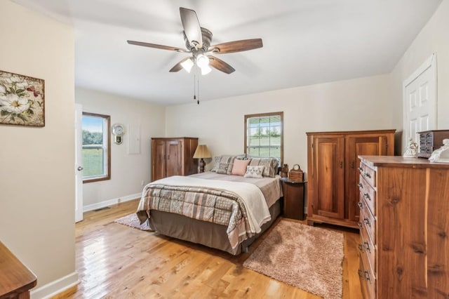 bedroom with light wood finished floors, multiple windows, a ceiling fan, and baseboards