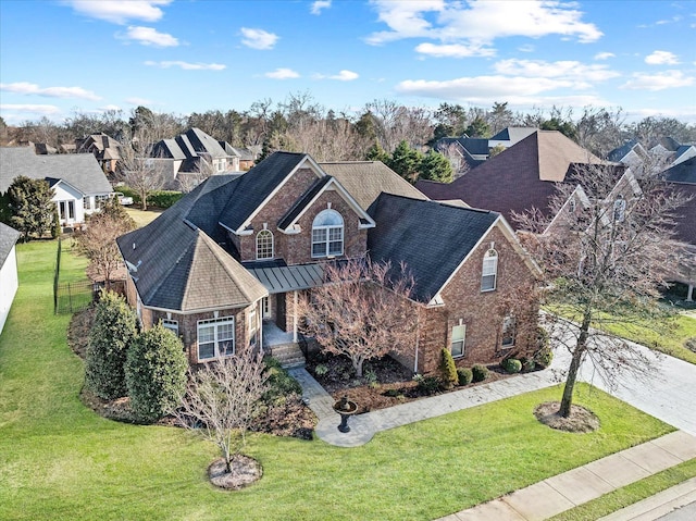 view of front of property featuring brick siding, concrete driveway, a standing seam roof, fence, and a front lawn