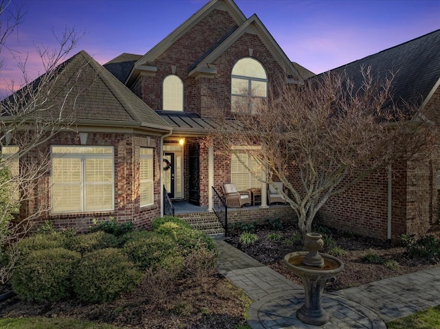 view of front of house with a shingled roof, a porch, and brick siding