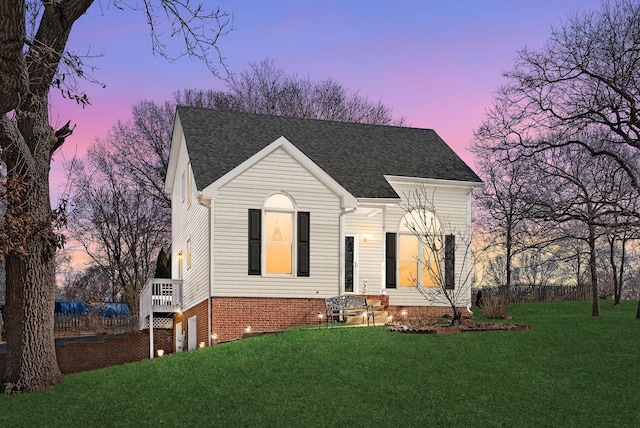 view of front of house with a shingled roof and a lawn