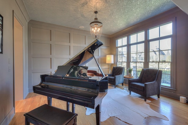 sitting room with a notable chandelier, a textured ceiling, a decorative wall, and wood finished floors