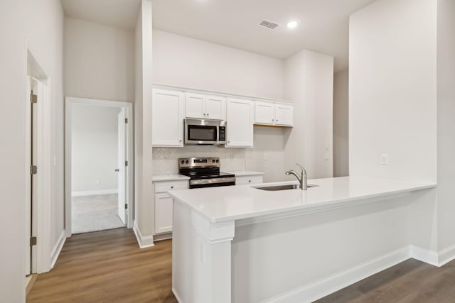 kitchen with a peninsula, a sink, visible vents, white cabinetry, and appliances with stainless steel finishes