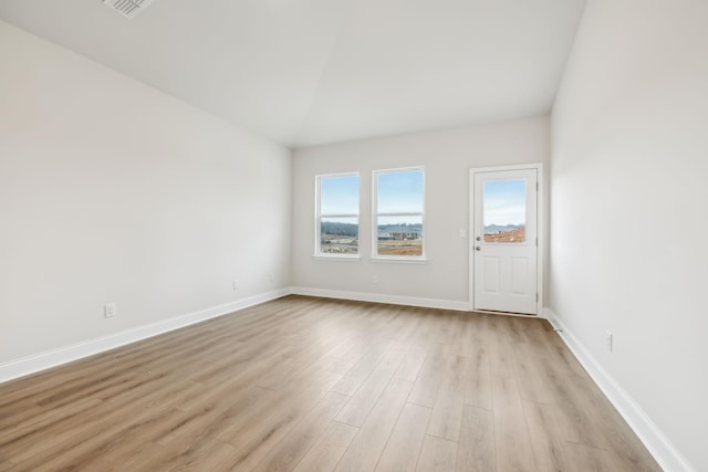 spare room featuring lofted ceiling, light wood finished floors, and baseboards