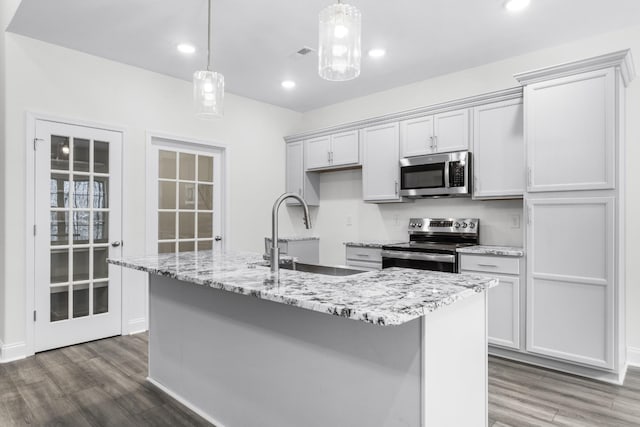 kitchen with stainless steel appliances, wood finished floors, a sink, and a center island with sink