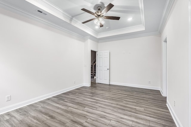 empty room with wood finished floors, visible vents, baseboards, a ceiling fan, and a tray ceiling