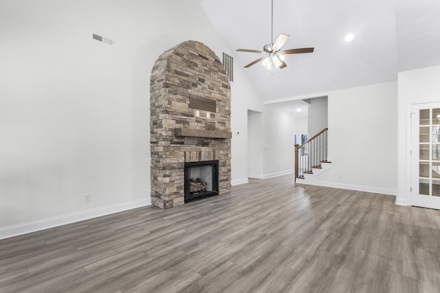 unfurnished living room featuring stairs, baseboards, wood finished floors, and a stone fireplace