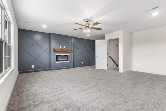 empty room with an accent wall, a fireplace, carpet flooring, visible vents, and baseboards