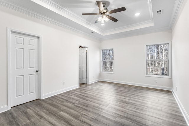 unfurnished bedroom featuring ornamental molding, a tray ceiling, wood finished floors, and baseboards