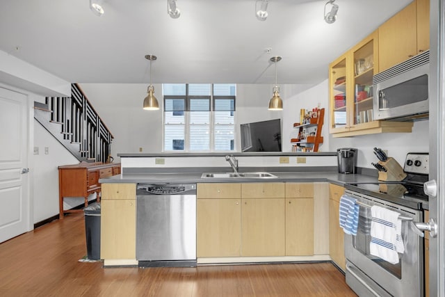 kitchen with light brown cabinets, stainless steel appliances, a peninsula, a sink, and light wood finished floors