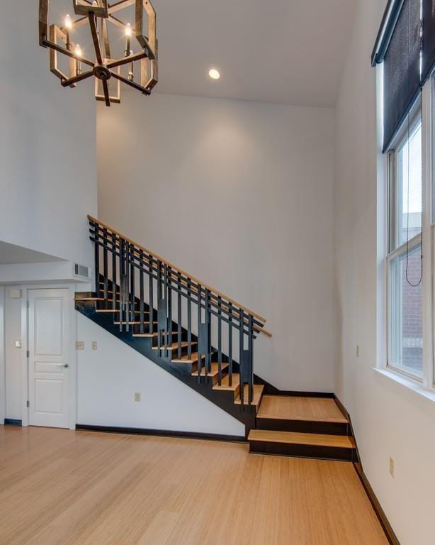 stairway with visible vents, a high ceiling, an inviting chandelier, wood finished floors, and baseboards