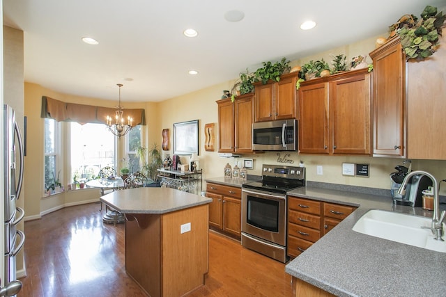 kitchen with stainless steel appliances, wood finished floors, a kitchen island, a sink, and brown cabinets