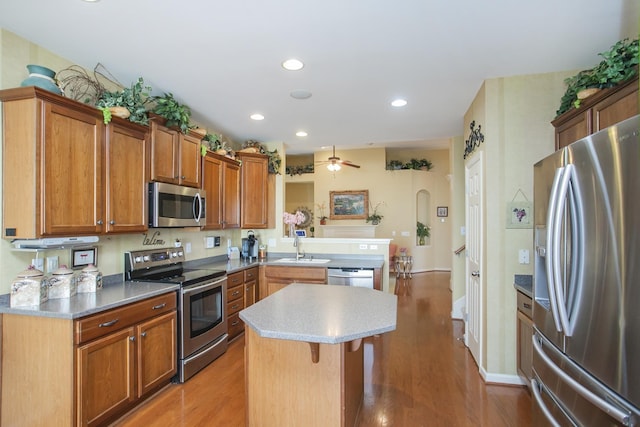 kitchen with stainless steel appliances, light wood-type flooring, a kitchen island, and a peninsula