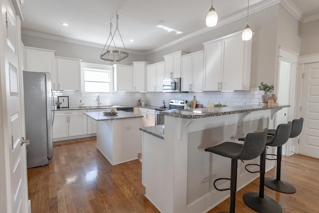 kitchen featuring stainless steel appliances, stone countertops, ornamental molding, wood finished floors, and a peninsula