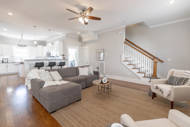 living room with baseboards, crown molding, light wood finished floors, and stairs