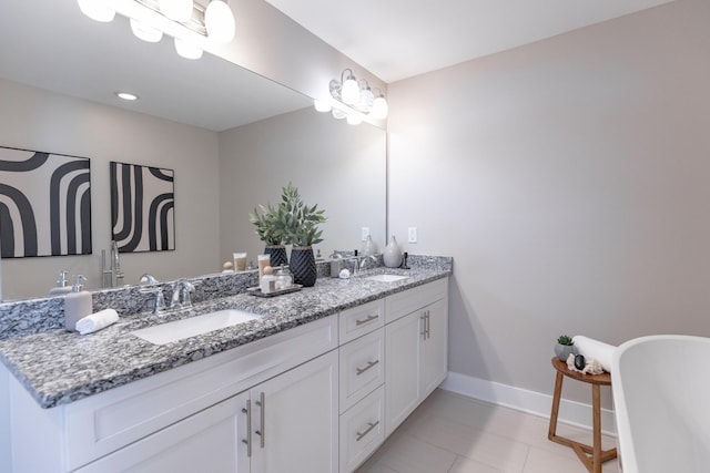 full bath with double vanity, a freestanding tub, baseboards, and a sink