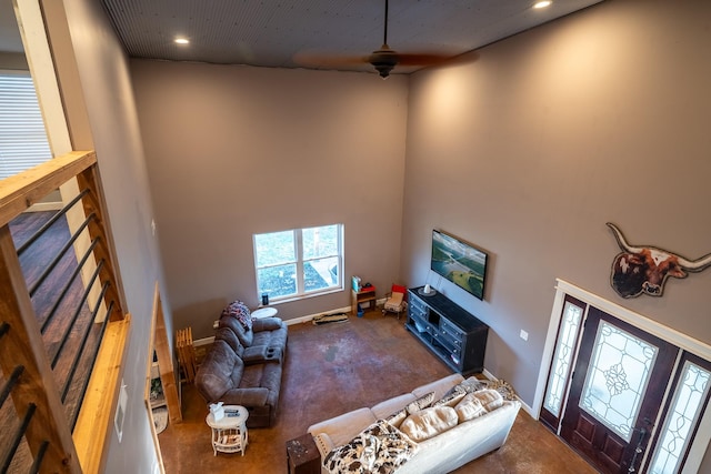 living area with ceiling fan, a towering ceiling, and baseboards