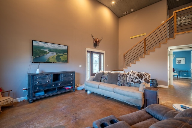 living area with baseboards, concrete floors, stairway, and a towering ceiling