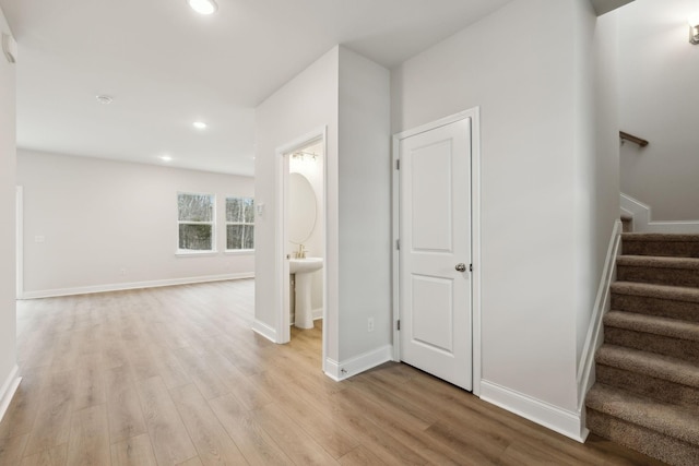 corridor with recessed lighting, light wood-style flooring, baseboards, and stairs