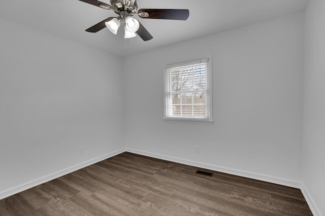 spare room featuring dark wood-type flooring, a ceiling fan, visible vents, and baseboards