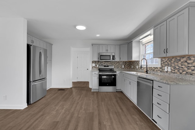 kitchen with light stone counters, dark wood-style flooring, tasteful backsplash, appliances with stainless steel finishes, and a sink