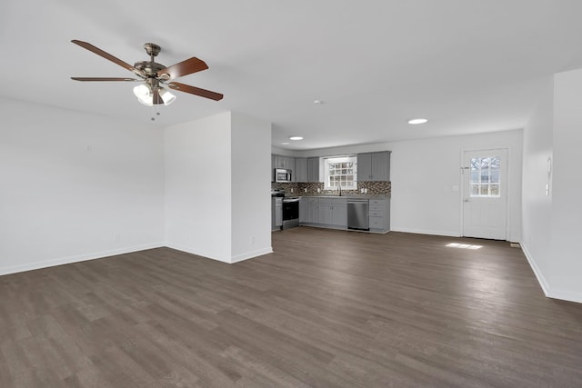 unfurnished living room featuring baseboards, dark wood-type flooring, and a healthy amount of sunlight