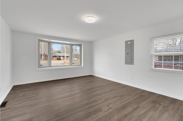 empty room featuring a wealth of natural light, dark wood-type flooring, visible vents, and electric panel