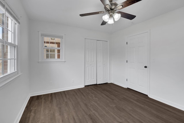 unfurnished bedroom with multiple windows, dark wood finished floors, and baseboards