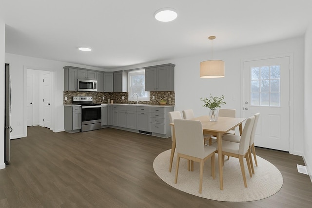 kitchen with decorative backsplash, appliances with stainless steel finishes, baseboards, dark wood-style flooring, and gray cabinets