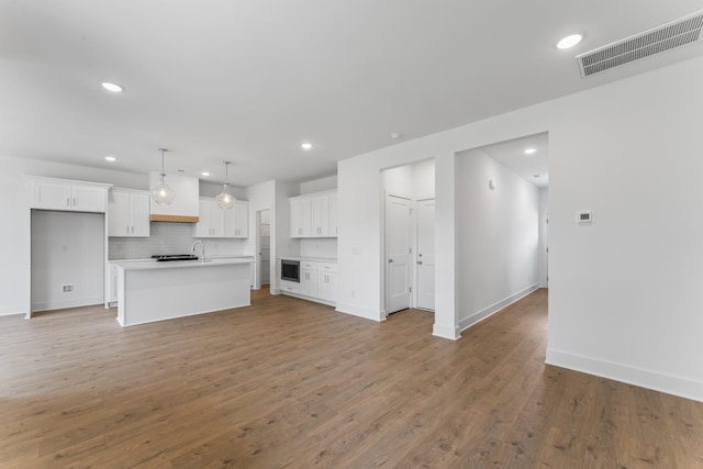 unfurnished living room with recessed lighting, visible vents, light wood-style flooring, a sink, and baseboards